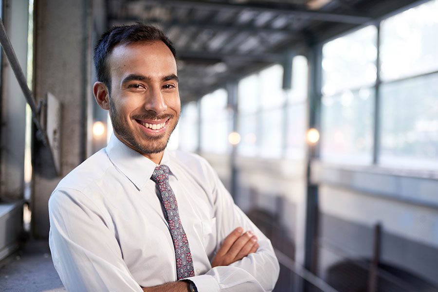 Business Insurance - Portrait of a Smiling Young Businessman Standing in an Empty Office Building with His Arms Crossed